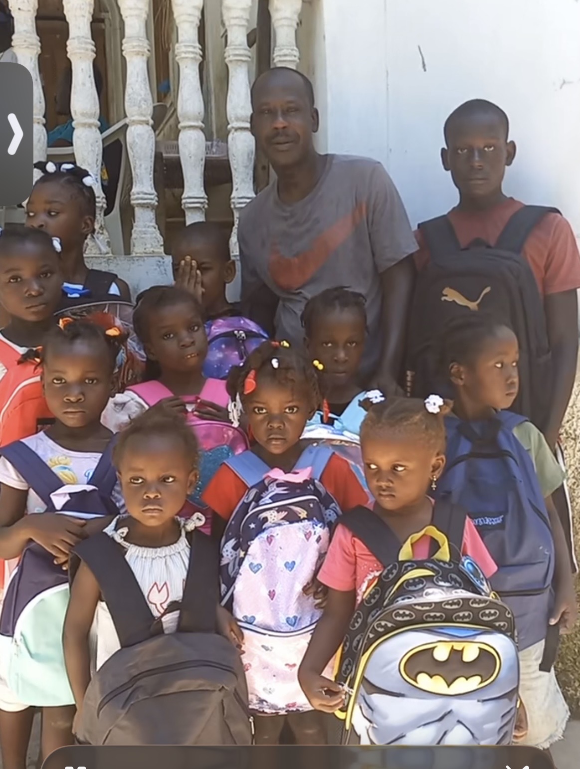 An adult standing with children carrying school backpacks.